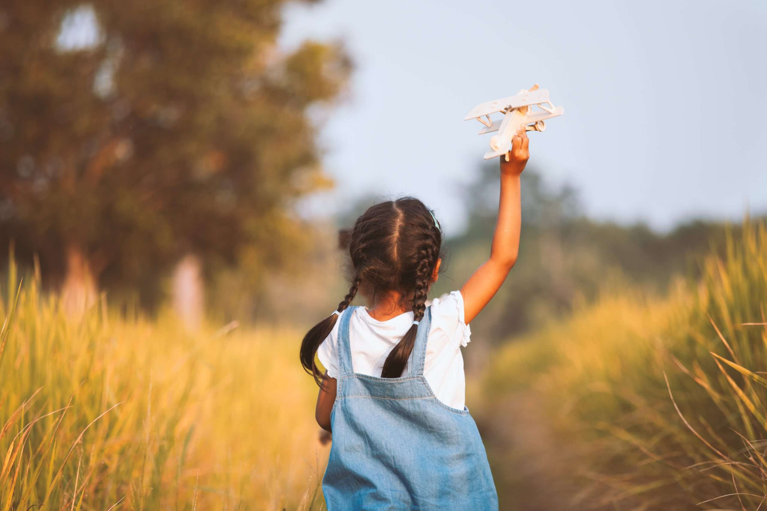 Cute asian child girl running and playing with toy wooden airplane in the field at sunset time with fun