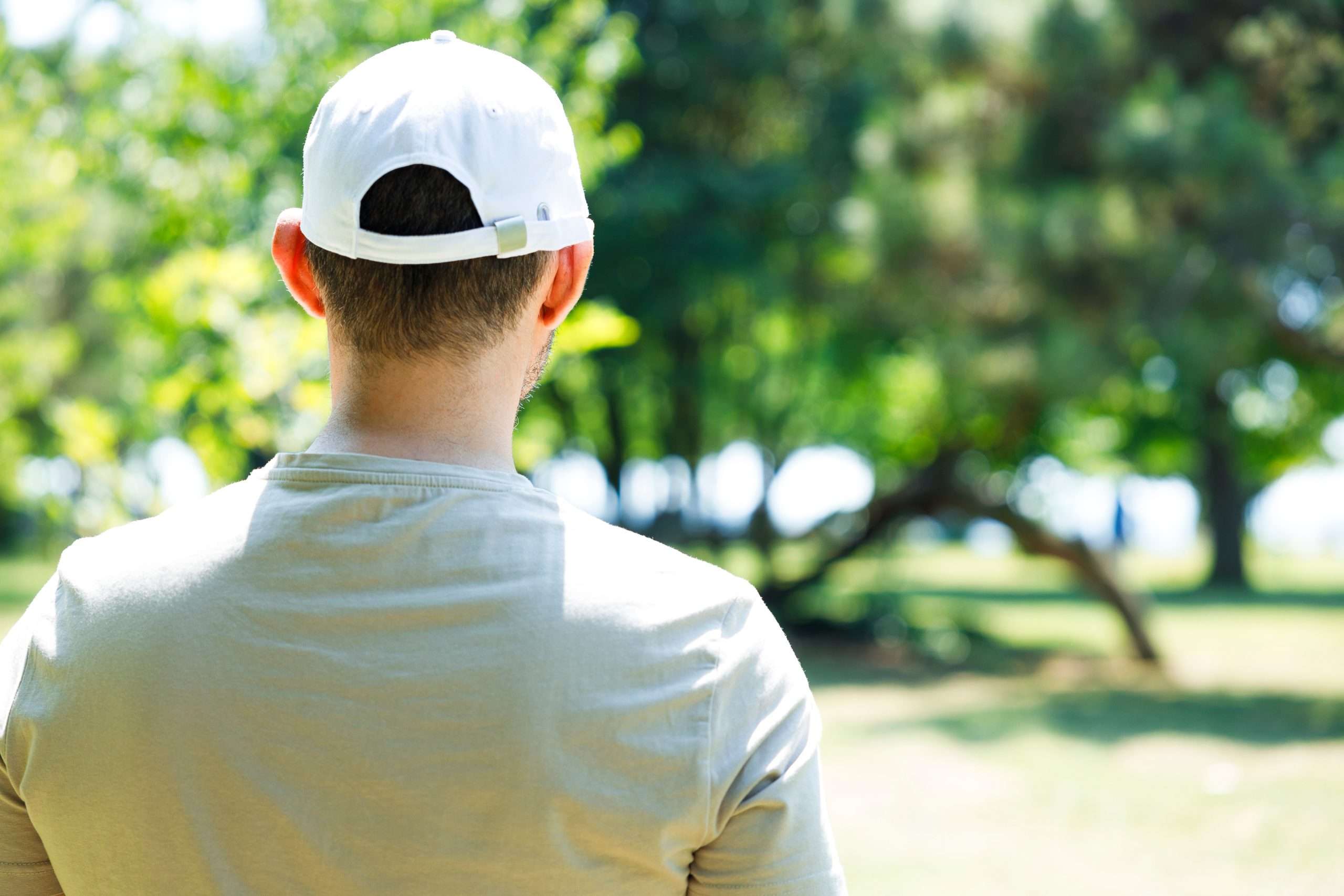 Back view of young man wearing a white baseball cap in the park