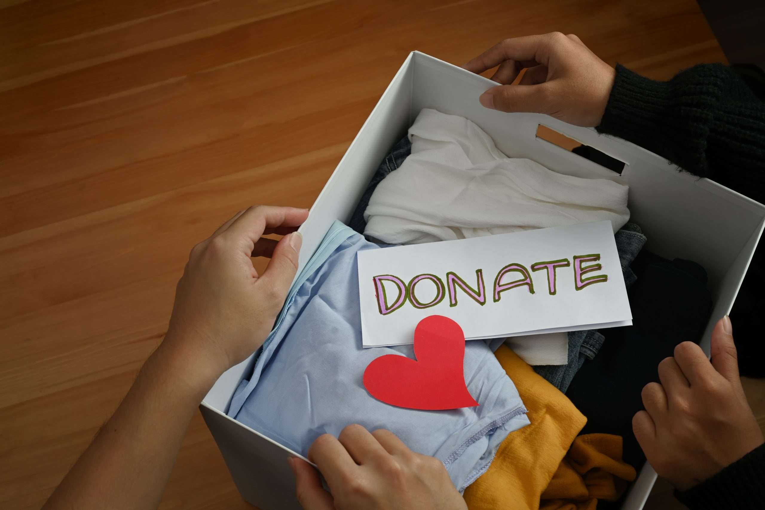 Top view of young volunteers holding box with clothes and donation lettering. Charity, donation and reuse recycle concept