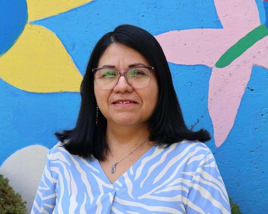 Portrait of Olga Muñoz in front of a colorful mural