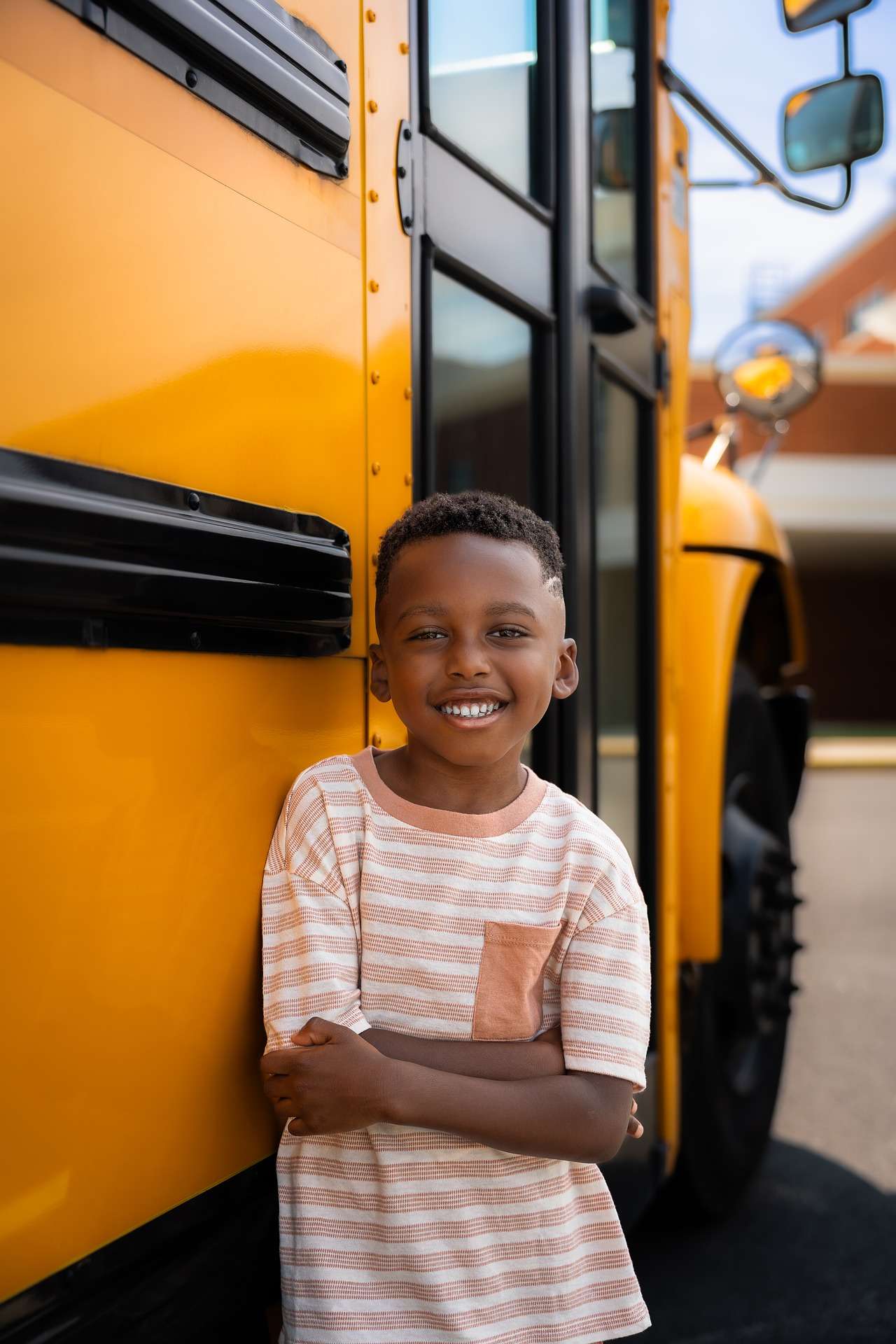 Smiling child standing beside a yellow school bus.