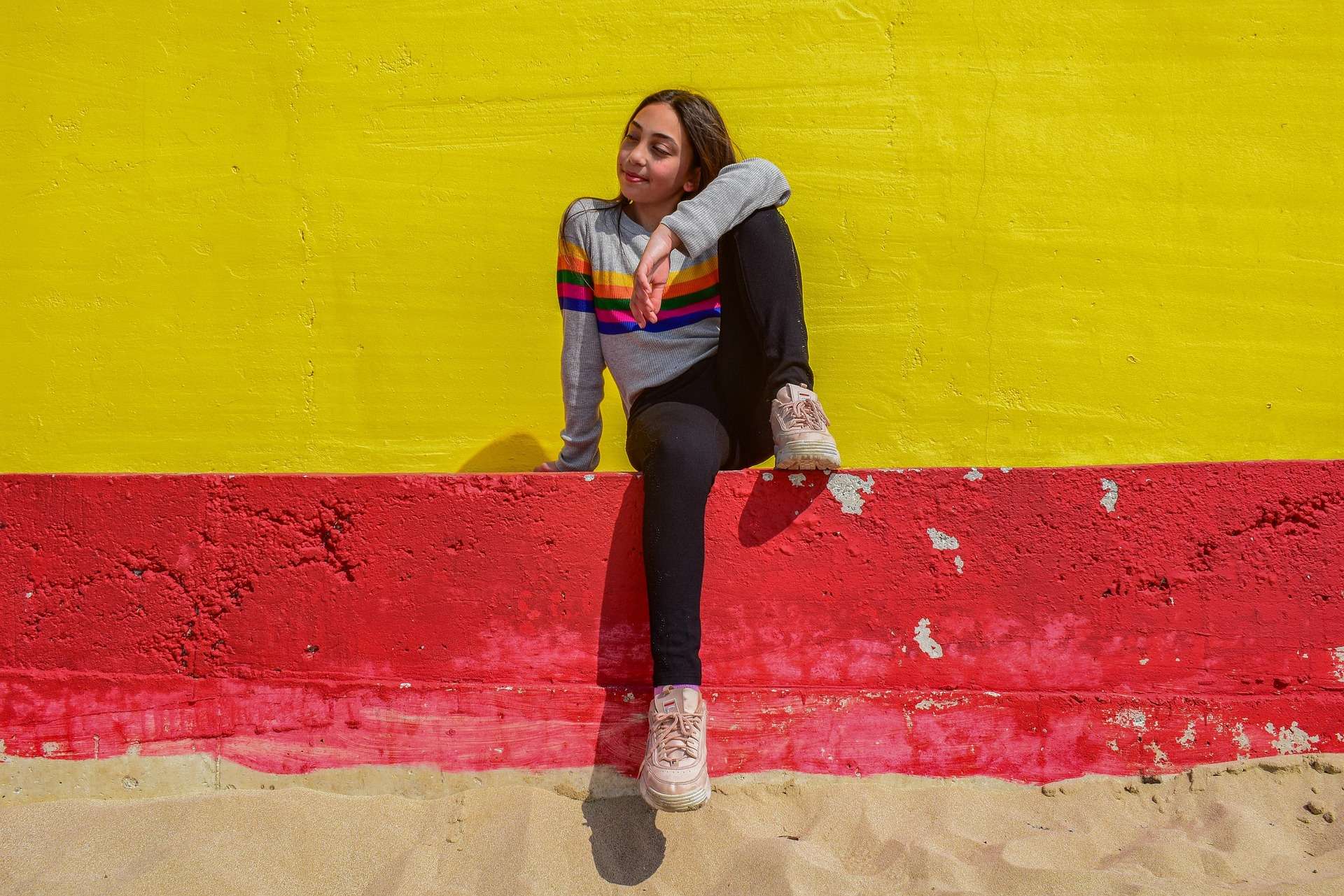 Teenager sitting against a bright yellow wall.